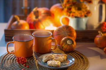 two orange cups  of tea and autumn decor with pumpkins, flowers and burning candles on table