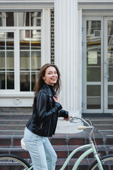 Obraz na płótnie Canvas young happy woman in stylish leather jacket riding bicycle