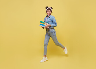 Happy Asian girl holding book and jumping over yellow background. back to school concept.