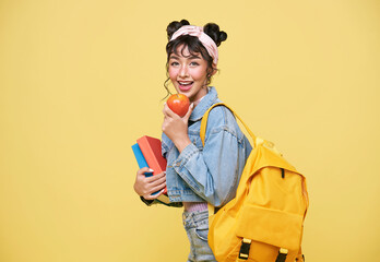 Happy Asian girl holding apple and notebook over yellow background. back to school concept.