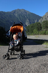 small child infant in the stroller with beautiful mountains on the background
