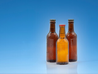 Three transparent brown beer bottles with water drops and cap on a blue background