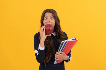 surprised kid hold copybooks for homework biting apple lunch on yellow background, back to school.