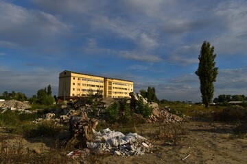 a yellow, lonely, abandoned, old, office building and a construction debris dump in front of it