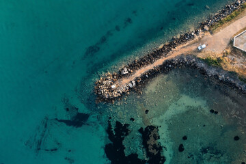 Top-down aerial view of a pier made of large stones going into the sea with clear turquoise water