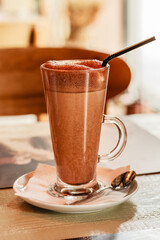 Delicious, natural cocoa drink with grated chocolate and milk in a glass mug on white plate. A mug of cacao