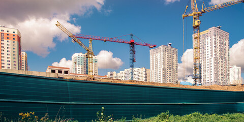 Textile canvas fixed on construction site fence behind working cranes. © Bonsales