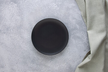 Black empty plate on gray concrete background with napkin.