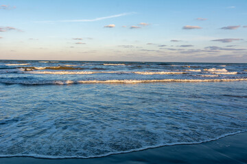 Sea, waves and a blue sky with small clouds in the beautiful light of the sunset