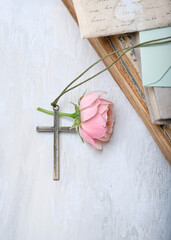 Christian metall cross, rose flower and old books on grey abstract background. cross, symbol of...