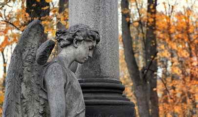 statue of sad angel on old cemetery, autumn natural background. Design for condolences, mourning...