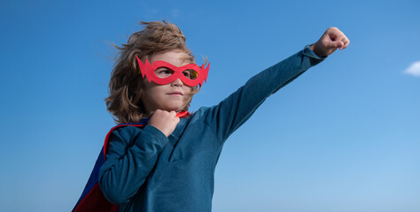 Seriuos child wearing a superhero costume. Super hero child against blue summer sky background. Kid having fun outdoors. Kids power concept.