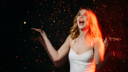Make wish. Happy woman. Christmas celebration. Holiday spirit. Excited beautiful laughing lady throwing golden confetti spangles isolated black long exposure red blur light copy space.