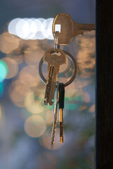 The keys with house keyring in the door keyhole with blurred night lights background, selective focus