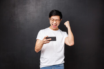 Technology, gadgets and people concept. Happy joyful lucky asian guy fist pump in celebration, hold...