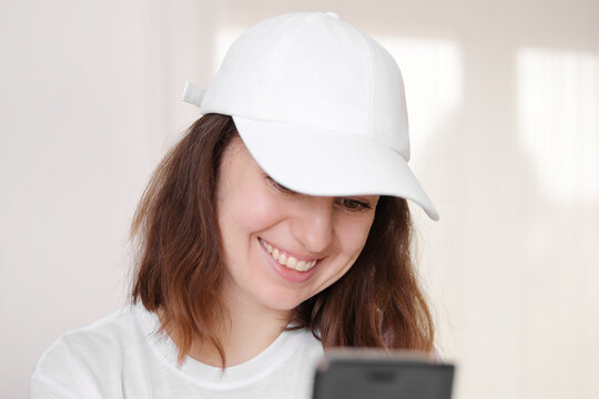 Female model wearing a white baseball cap. White cap mockup, template for picture, text or logo. Girl with a cap holding smarthphone. Free space, copy space.