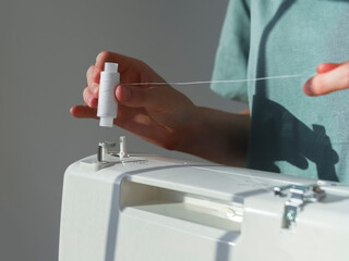 Hands putting thread spool on sewing machine.