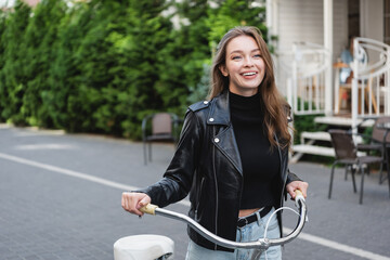 cheerful young woman standing near bicycle on urban street of europe