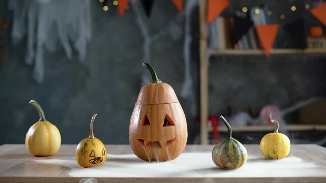 A pumpkin lantern on the table in the room. Halloween pumpkin with smoke from his eyes and a scary smile.