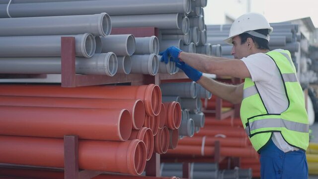 Warehouse employee choosing plastic pipe carrying manufactured product on shoulder walking away leaving in slow motion. Portrait of Middle Eastern man working outdoors at storage on sunny day