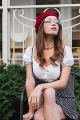 pretty young woman in red beret and eyeglasses sitting on chair outside