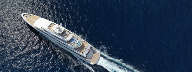 Aerial drone ultra wide panoramic photo of beautiful modern super yacht with wooden deck cruising in high speed deep blue open ocean sea