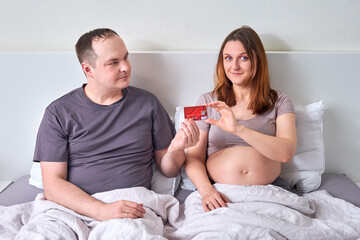 Obraz na płótnie Canvas A man gives a pregnant woman a bank card. Husband gives his wife a credit card during her pregnancy