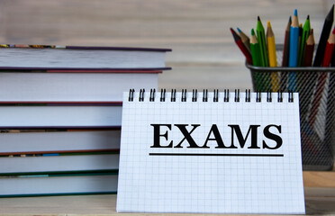 EXAMS - word in a notebook against the background of books and pencils