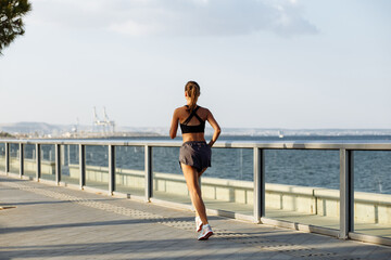 beautiful fitness girl in shorts and sports top running on the waterfront by the sea in sunny weather