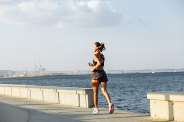 beautiful fitness girl in shorts and sports top running on the waterfront by the sea in sunny weather