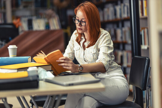 Red hair female student reading a book at the college library.