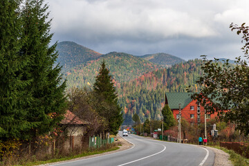 Zakarpattia Oblast, Ukraine - A road in a small village located in a mountain valley. The sun's rays make their way through the thunderclouds. The tops of high mountains are hidden by clouds.