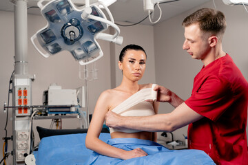 Surgeon with woman patient in operating room before breast augmentation for girl. Doctor wraps...