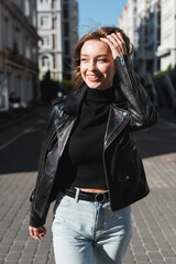 happy young woman in leather jacket standing on urban street