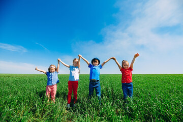 Happy Children on a green field with their hands up.
