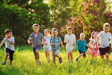 A group of happy children of boys and girls run in the Park on the grass on a Sunny summer day.