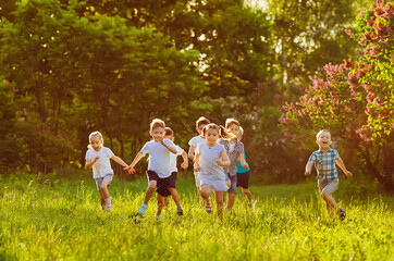 A group of happy children of boys and girls run in the Park on the grass on a Sunny summer day.