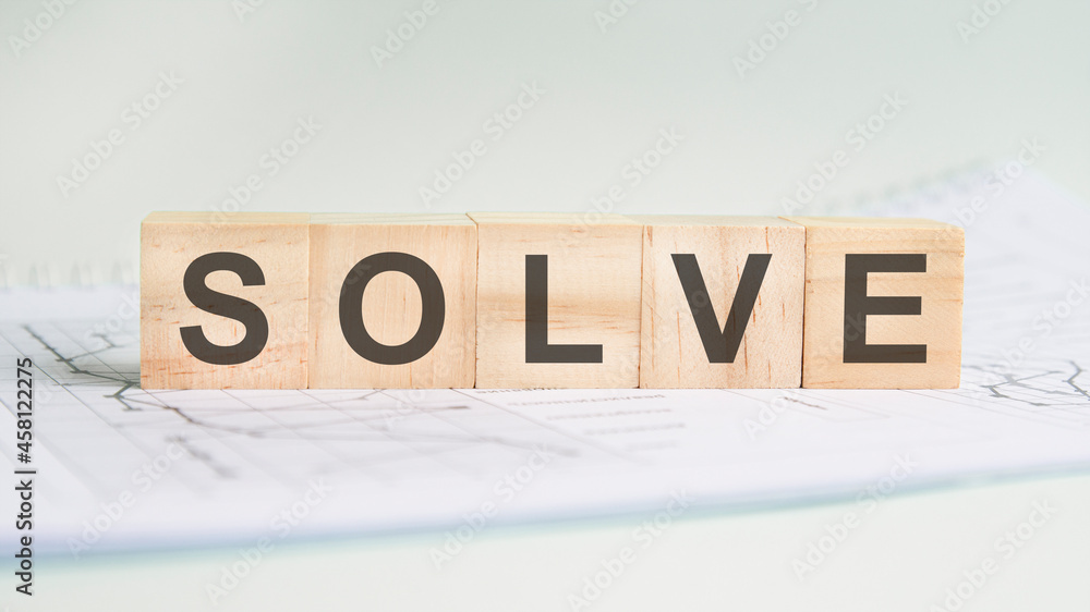 Poster solve is written on light wooden blocks. the word is located on a sheet with charts and graphs