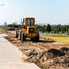 A wheeled bulldozer clears the ground with a metal shield. Road construction works.