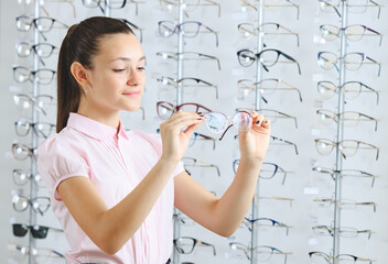 Woman choosing the glasses in optics store, eyesight and vision concept.