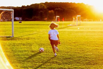 Young girl kicking a soccer ball at sunset on the soccer field 