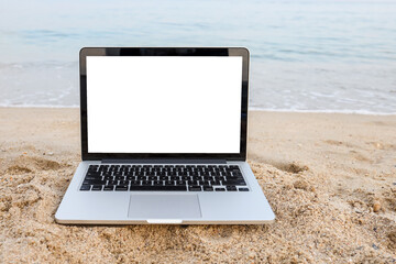 Laptop on sand at summer beach in background with white screen.