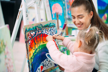 Mother and daughter painting together. Adult woman helping to child girl.