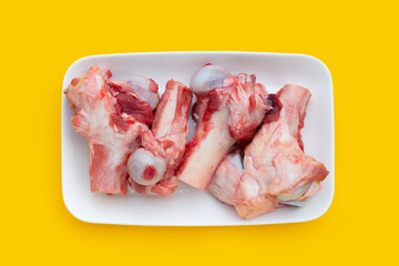 Raw pork bones in white plate on yellow background.
