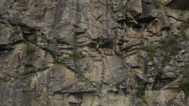 Strong muscular man rock climber, rappels down and removes the quickdraw on the hooks. successful completion of the climbing route. Outdoor rock climbing and active lifestyle concept, drone shot