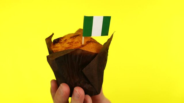 Cupcake with Nigerian flag on male palm against yellow background