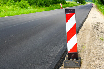 a new asphalt road in a rural area with a red and white warning sign in the foreground