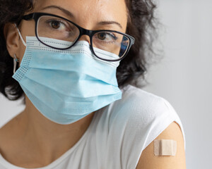 young woman in mask with plaster on her shoulder, after vaccination