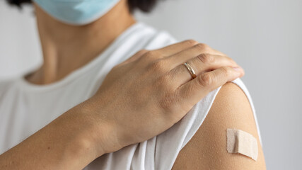 young woman in mask with plaster on her shoulder, after vaccination