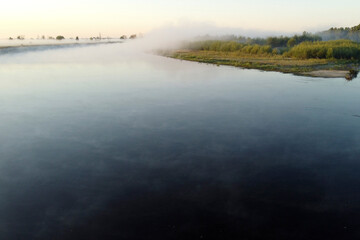 Mist covers the river, trees, and land at dawn. Autumn photos of fog taken with drone